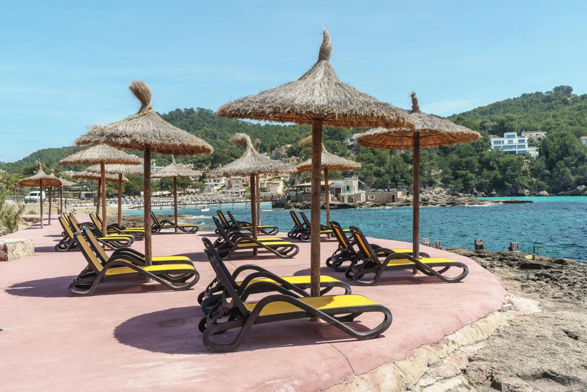 Transats jaunes sous des parasols de paille sur une terrasse ensoleillée face à la mer.
