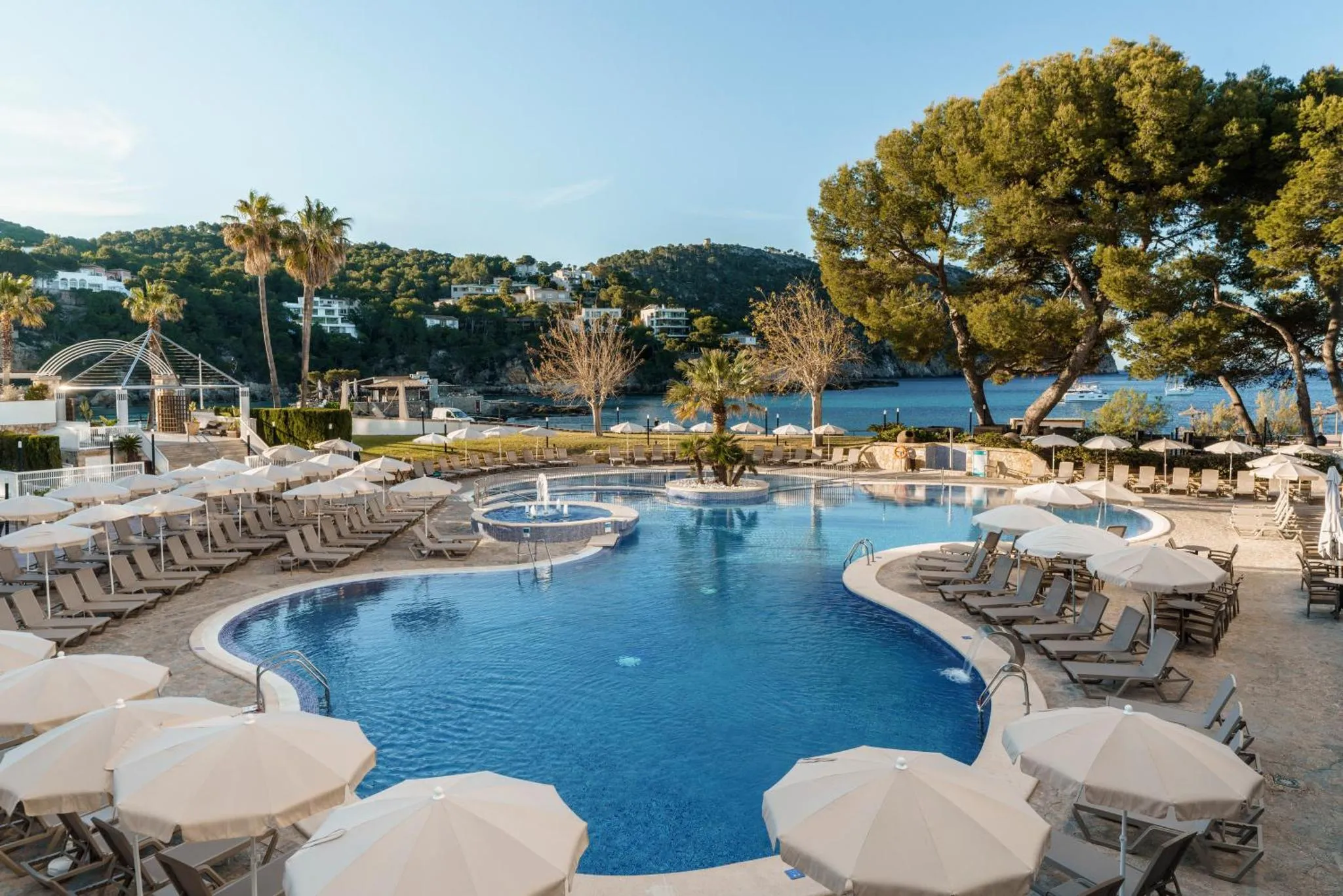 Piscine extérieure avec transats et parasols, vue sur la mer et la végétation.