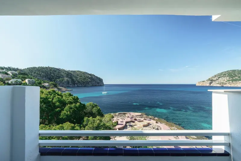 Vue dégagée sur une crique turquoise et une côte verdoyante depuis un balcon.