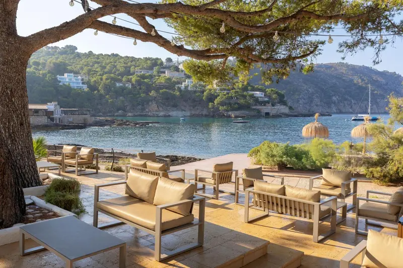 Terrasse aménagée avec des canapés et des tables basses face à une crique.