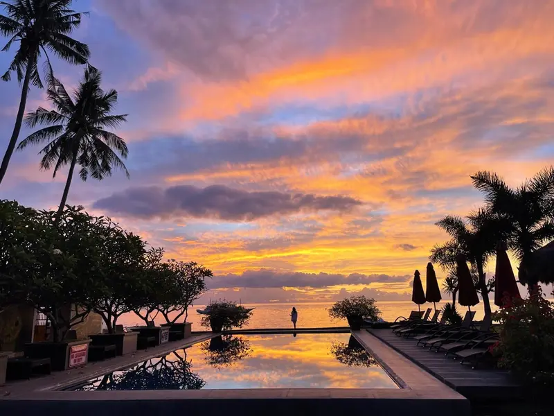 Coucher de soleil flamboyant sur l'océan, avec des palmiers et une piscine au premier plan.
