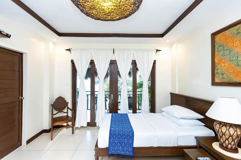 Une chambre lumineuse avec un lit recouvert d'une courtepointe bleue et une chaise en bois.