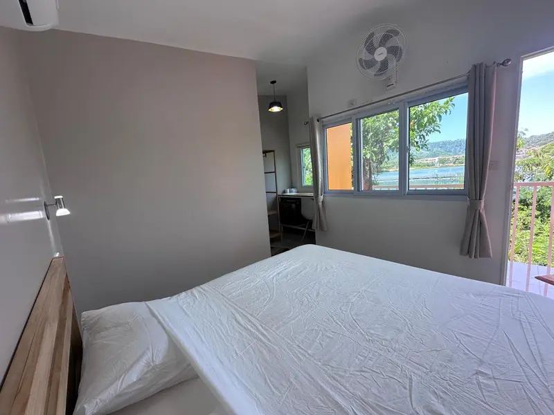 Une chambre lumineuse avec un lit blanc et une vue sur un paysage verdoyant.
