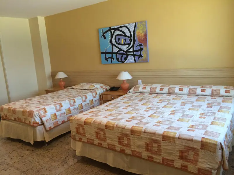 Deux lits simples dans une chambre aux murs jaunes et au sol carrelé.