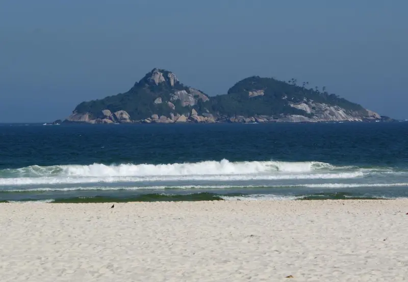 Une plage de sable fin avec des vagues et une île rocheuse en arrière-plan.
