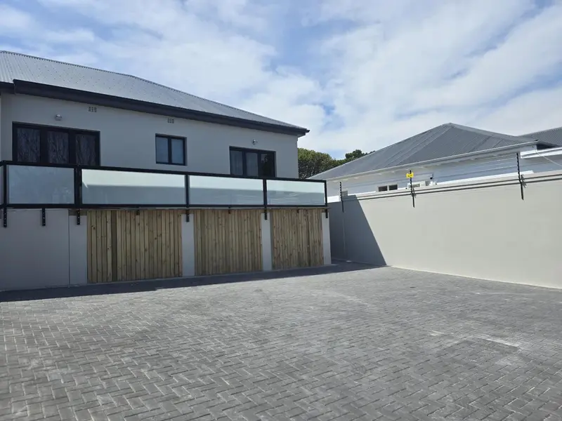 Façade d'un bâtiment avec une terrasse et un parking pavé.