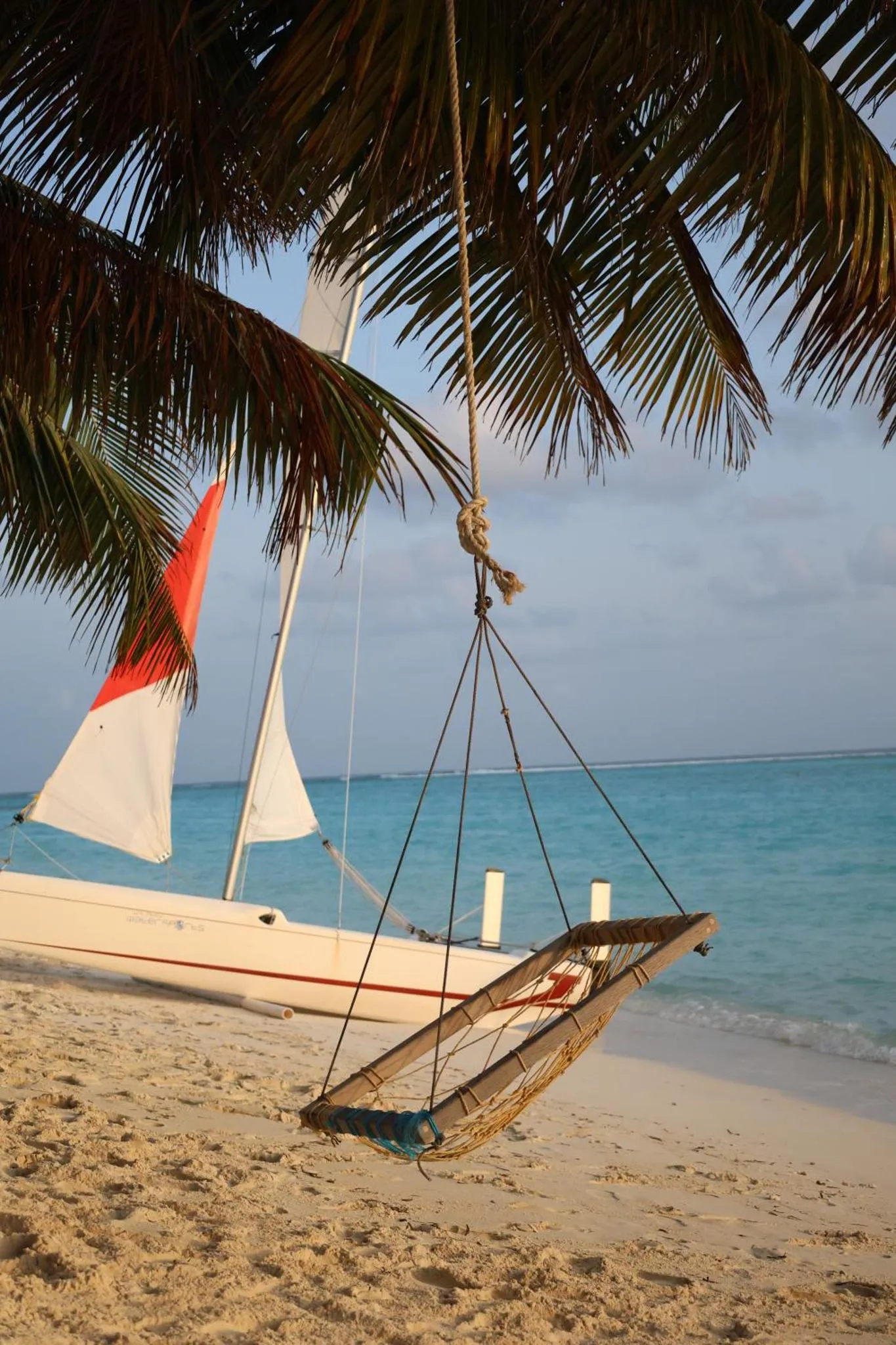 Un hamac est suspendu entre un palmier et un bateau sur une plage de sable clair.