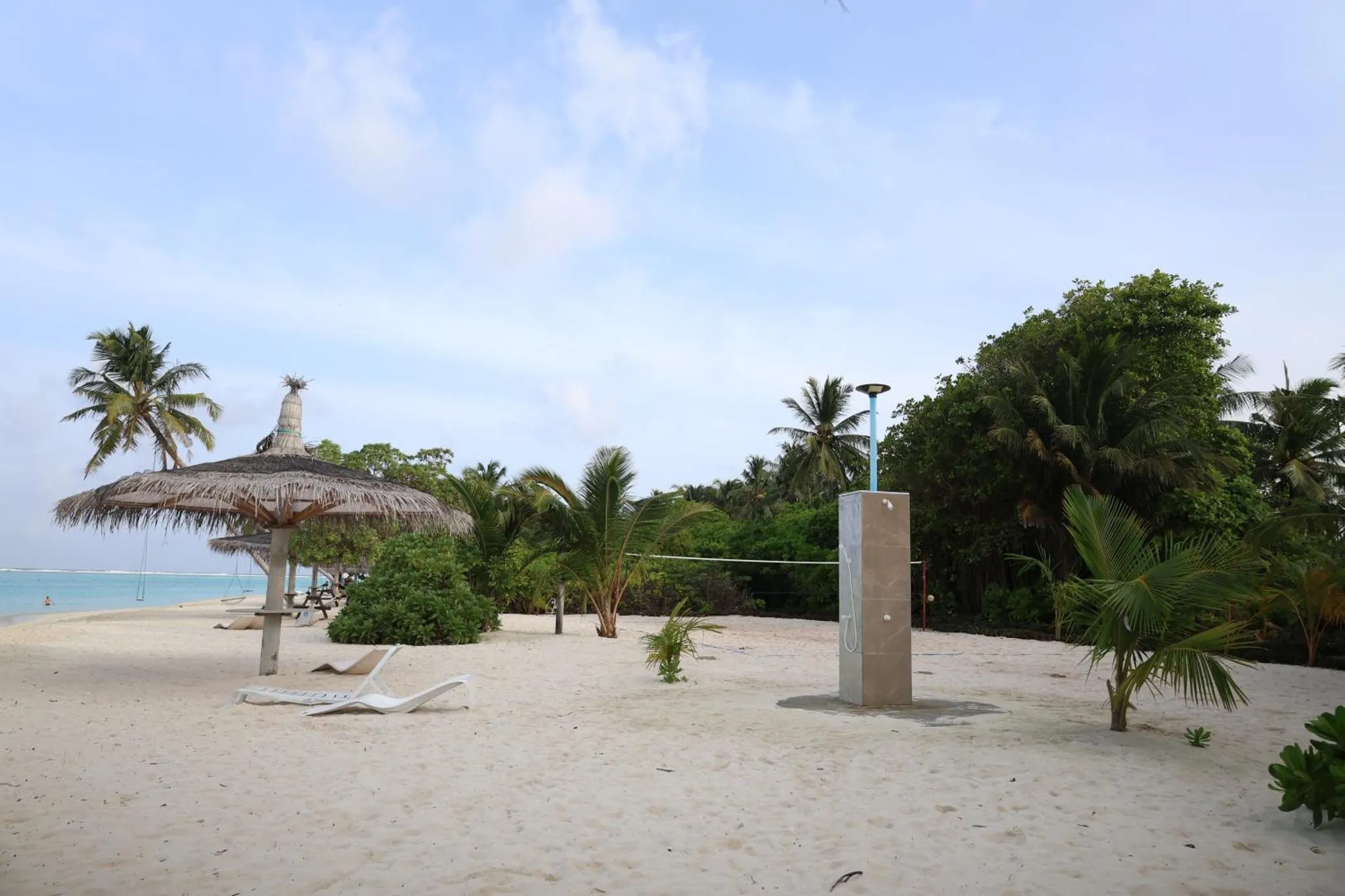 Plage de sable blanc avec parasols en chaume et végétation tropicale.