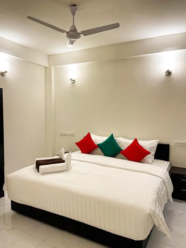 Une chambre lumineuse avec un grand lit recouvert d'une courtepointe blanche et de coussins colorés.