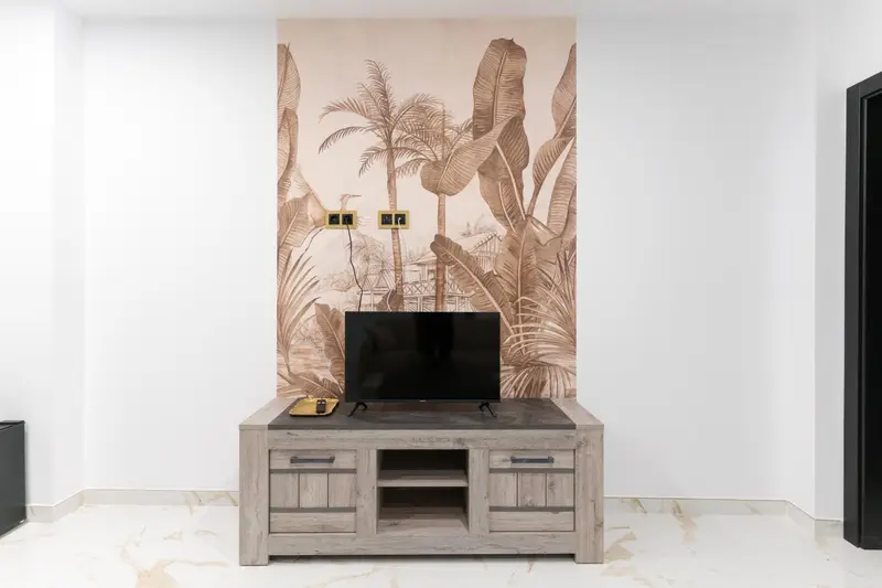 Un meuble bas en bois supporte un téléviseur mural sur un fond de palmiers stylisés.
