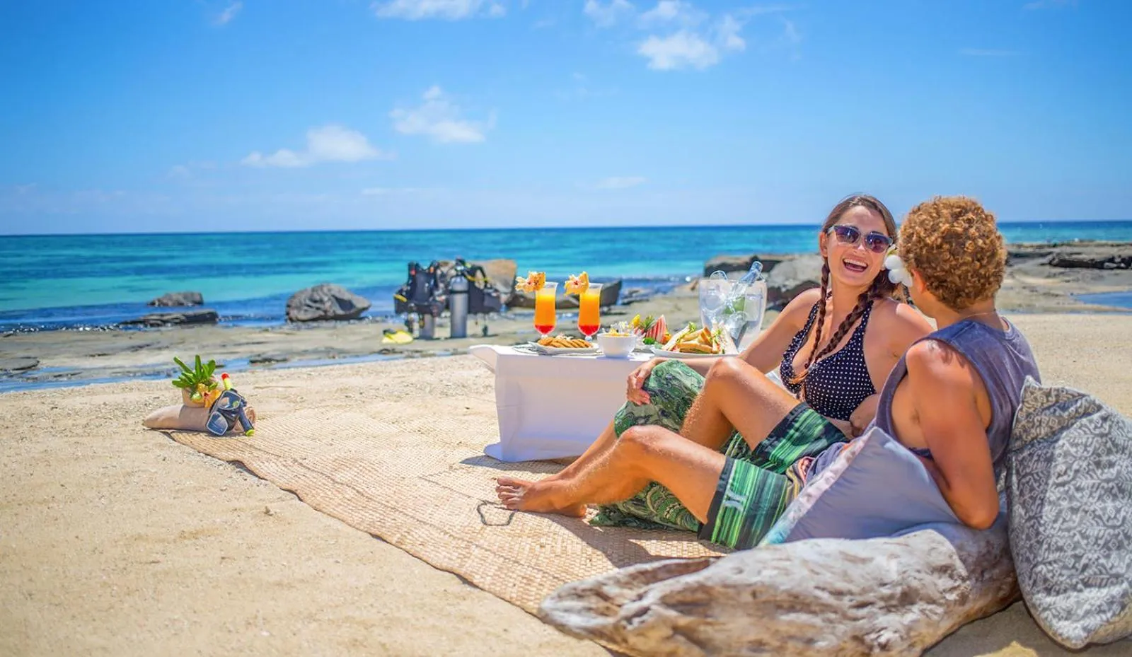 Un couple se détend sur une plage de sable blanc avec des boissons et des collations.