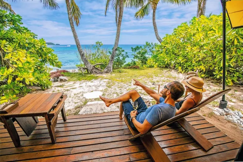 Un couple se détend sur une terrasse en bois face à une plage tropicale.