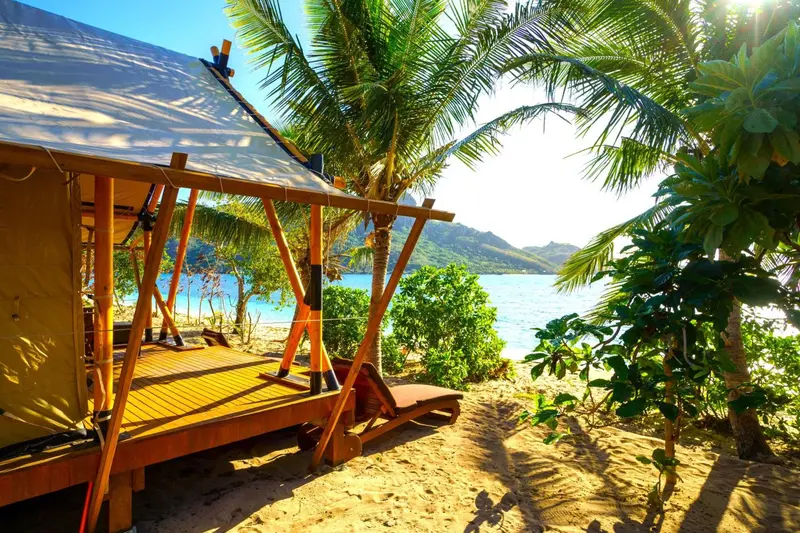 Une terrasse en bois ombragée surplombe une plage de sable fin.