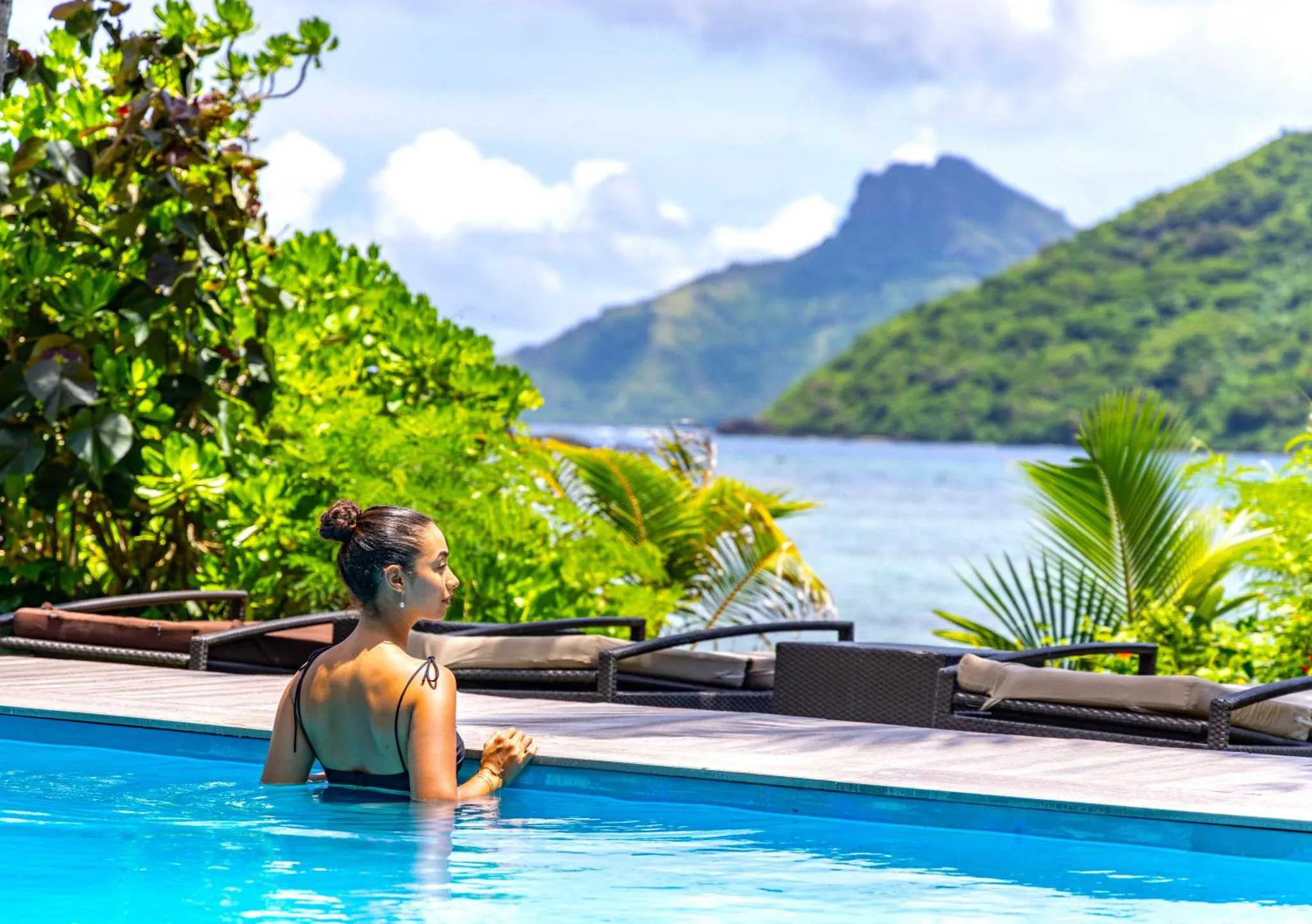 Une femme se tient au bord d'une piscine avec vue sur la mer et les montagnes.