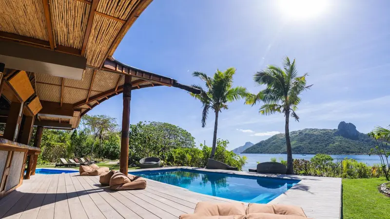 Terrasse ombragée avec piscine et vue sur la végétation tropicale et la mer.