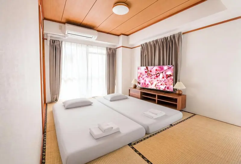 Chambre lumineuse avec deux lits simples et un téléviseur mural.