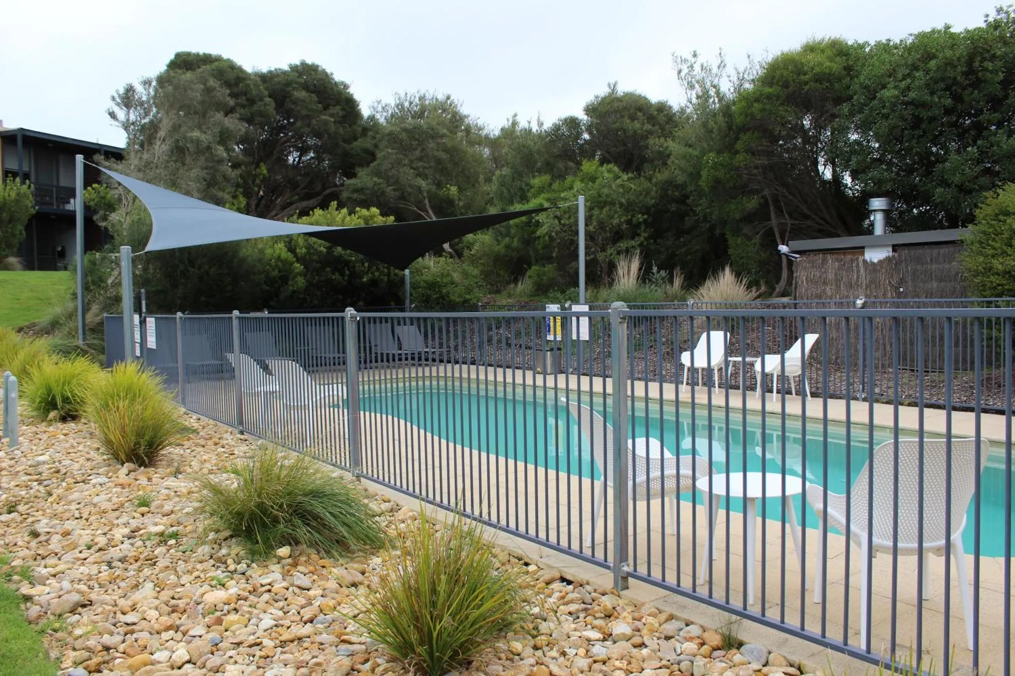 Une piscine rectangulaire est entourée d'une terrasse avec des chaises longues et protégée par une clôture.