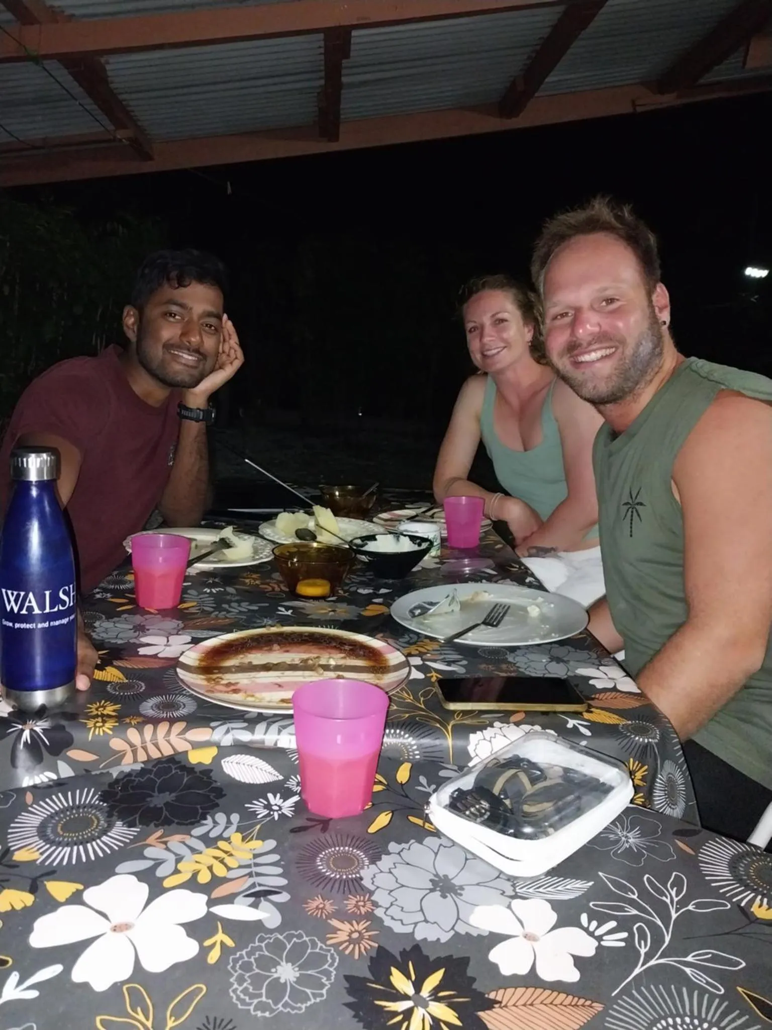 Trois personnes sourient autour d'une table garnie de plats et de boissons.