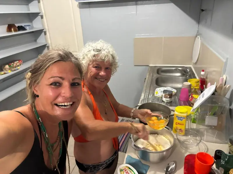 Deux femmes sourient en préparant un plat dans une cuisine lumineuse.