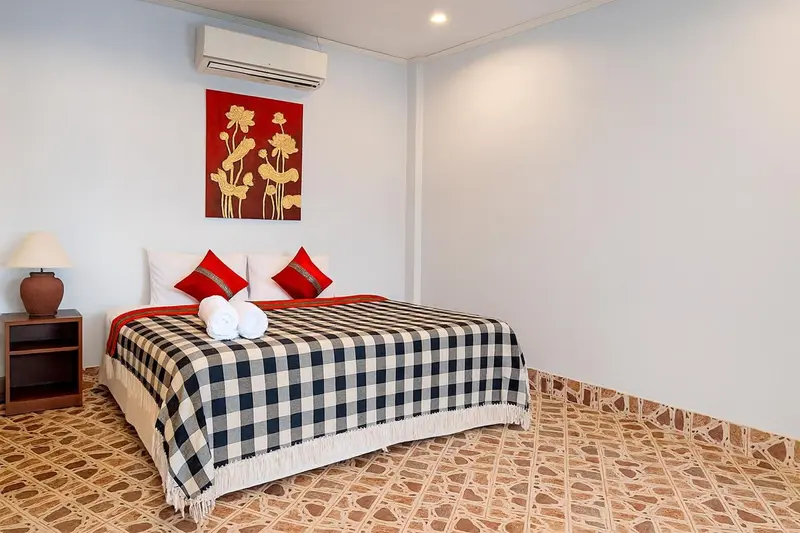 Une chambre lumineuse avec un lit recouvert d'une courtepointe à carreaux et décorée de coussins rouges.