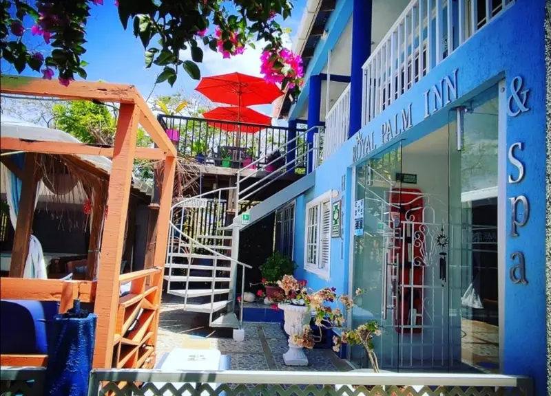 Façade d'un bâtiment bleu avec une végétation luxuriante et des parasols rouges.