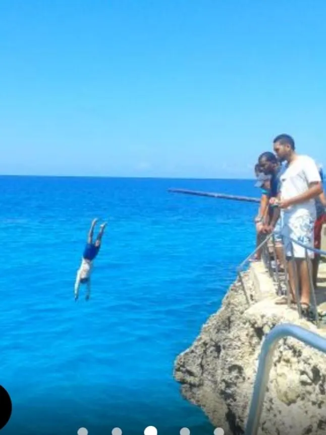 Une personne plonge d'une falaise rocheuse en bord de mer, observée par des spectateurs.