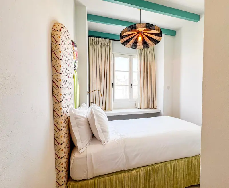 Une chambre lumineuse avec un lit recouvert de coussins blancs et une tête de lit décorative.