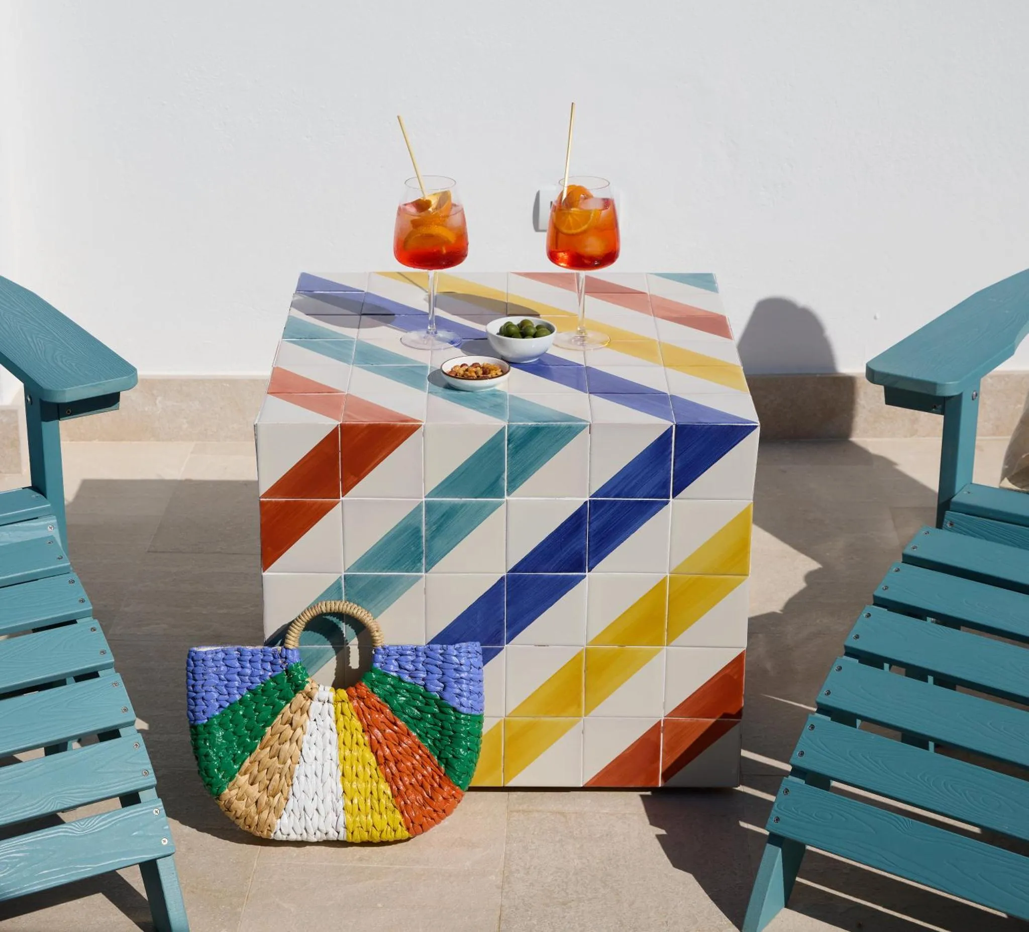 Une table colorée et des chaises en bois sur une terrasse ensoleillée.
