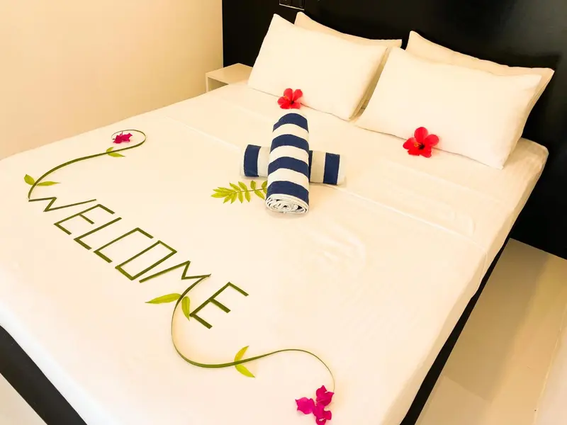 Un lit double est soigneusement fait avec une décoration florale et une serviette roulée.