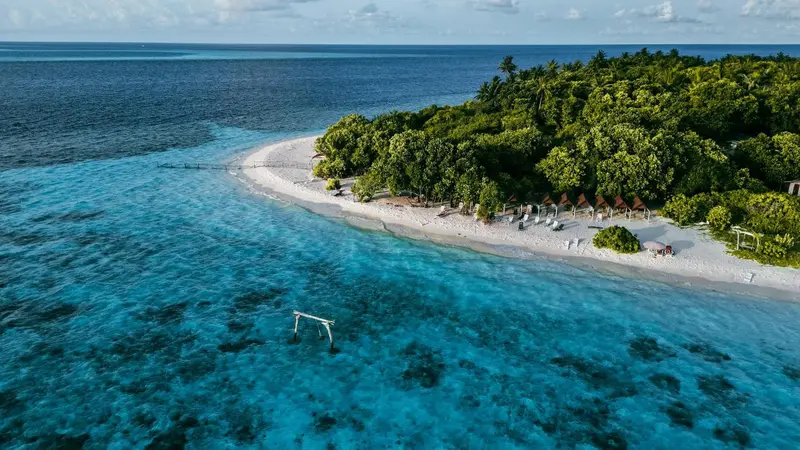 Vue aérienne d'une plage de sable blanc bordée de végétation luxuriante et d'une mer turquoise.