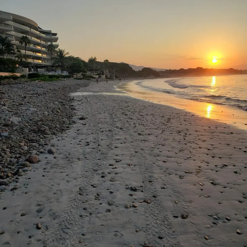 Plage de galets au coucher du soleil, avec une vue sur un bâtiment et la mer.