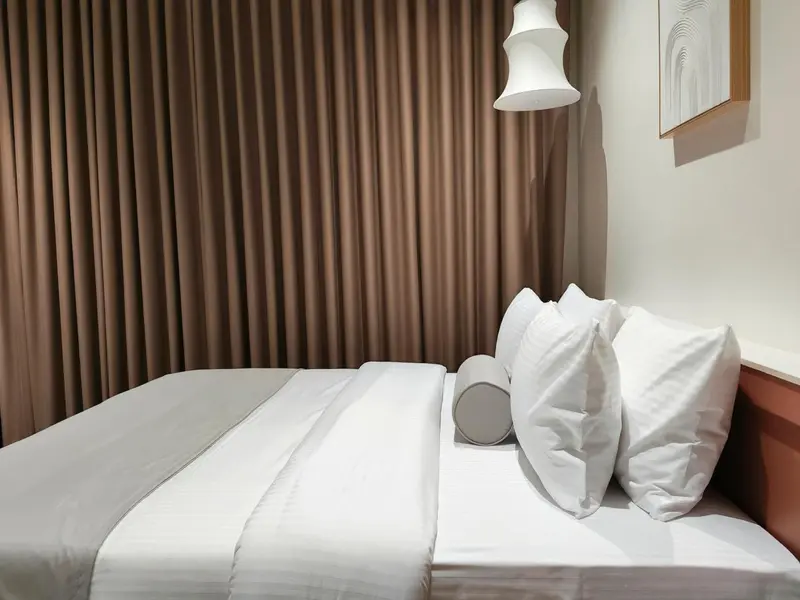 Un lit blanc est fait dans une chambre aux rideaux beiges.