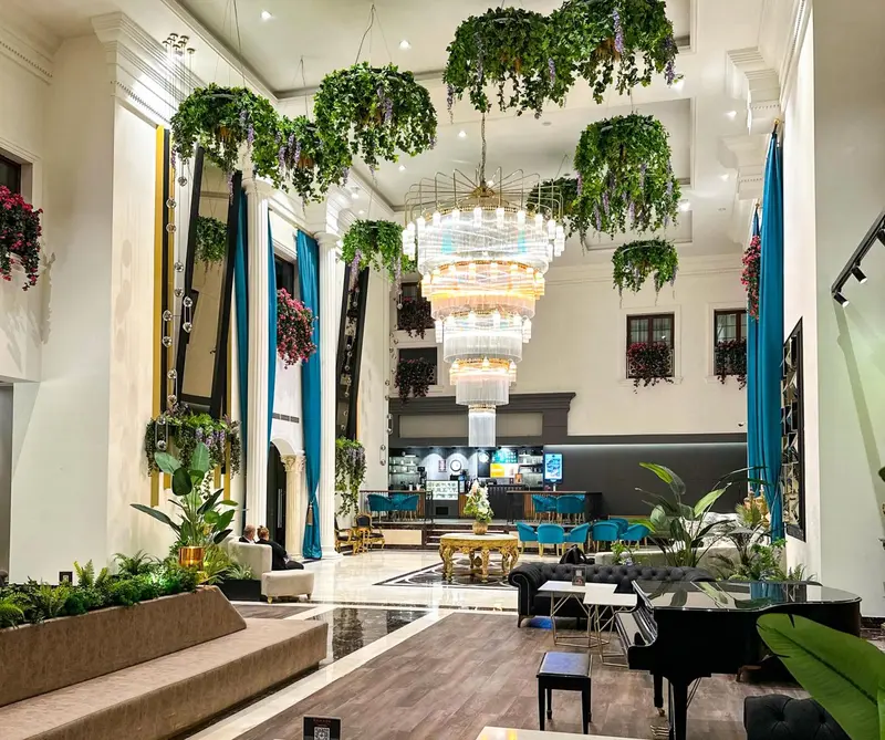 Vaste hall d'accueil décoré de plantes suspendues et illuminé par un grand lustre.