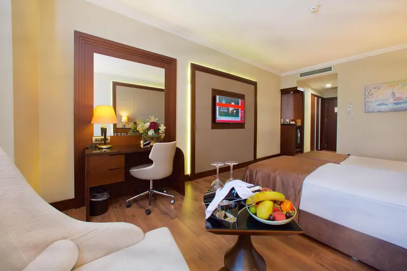 Une chambre d'hôtel lumineuse avec un bureau et un lit décoré de fruits.