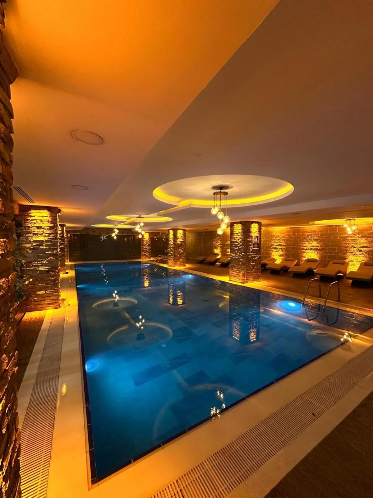 Une piscine intérieure illuminée aux tons chauds, avec des chaises longues sur le côté.