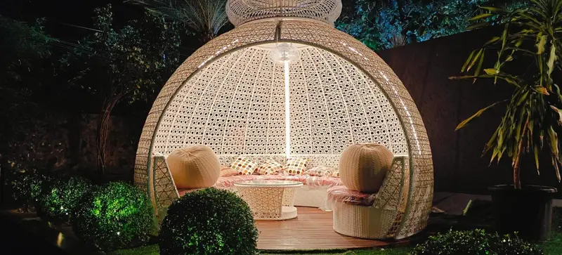 Un salon de jardin en osier illuminé se trouve dans un espace extérieur verdoyant.