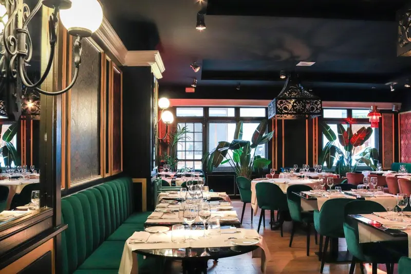 Une salle de restaurant élégante avec des tables dressées et des banquettes vertes.