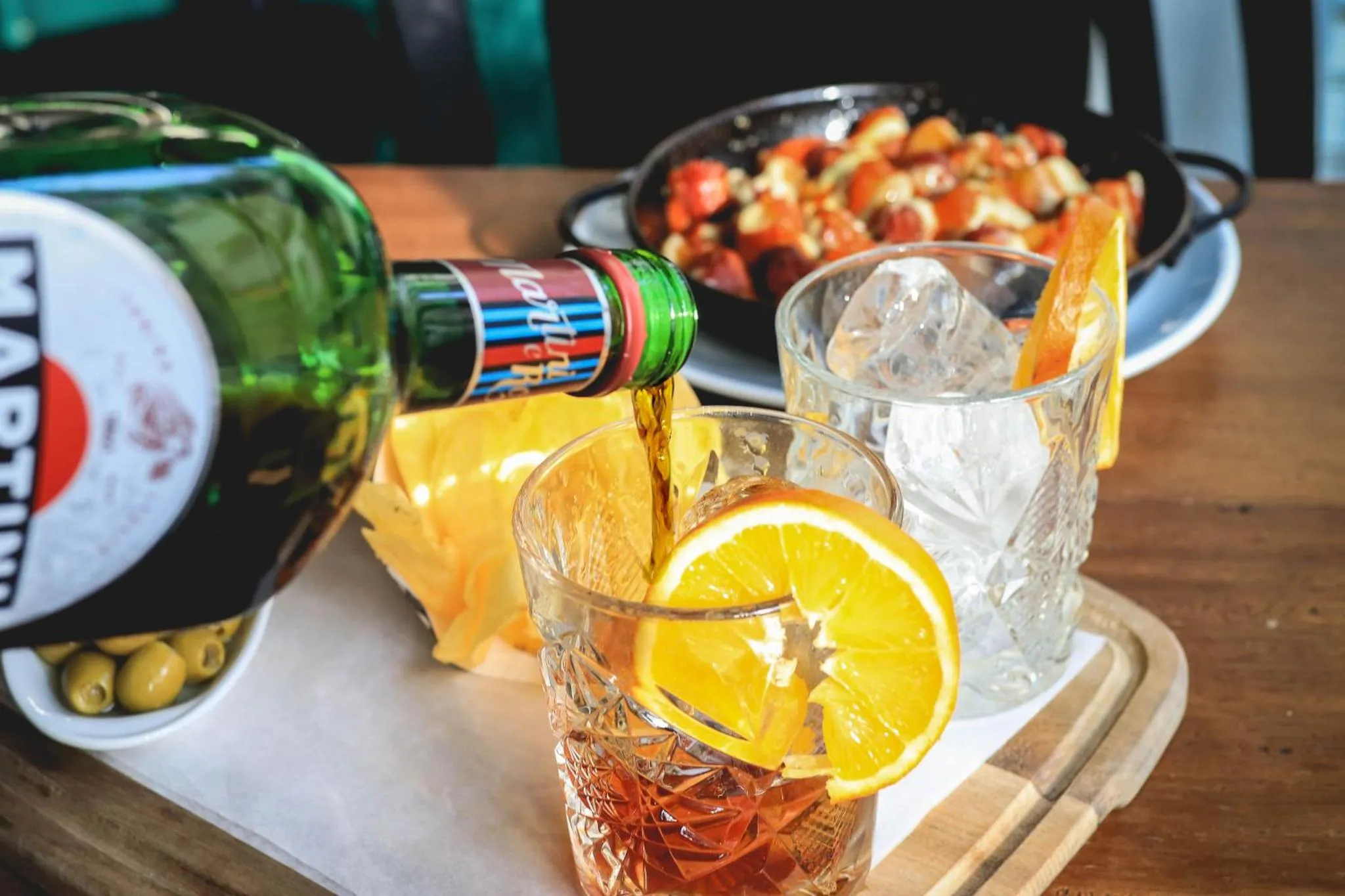 Une bouteille de Martini et des verres de cocktails sont servis avec des olives et des tranches d'orange.