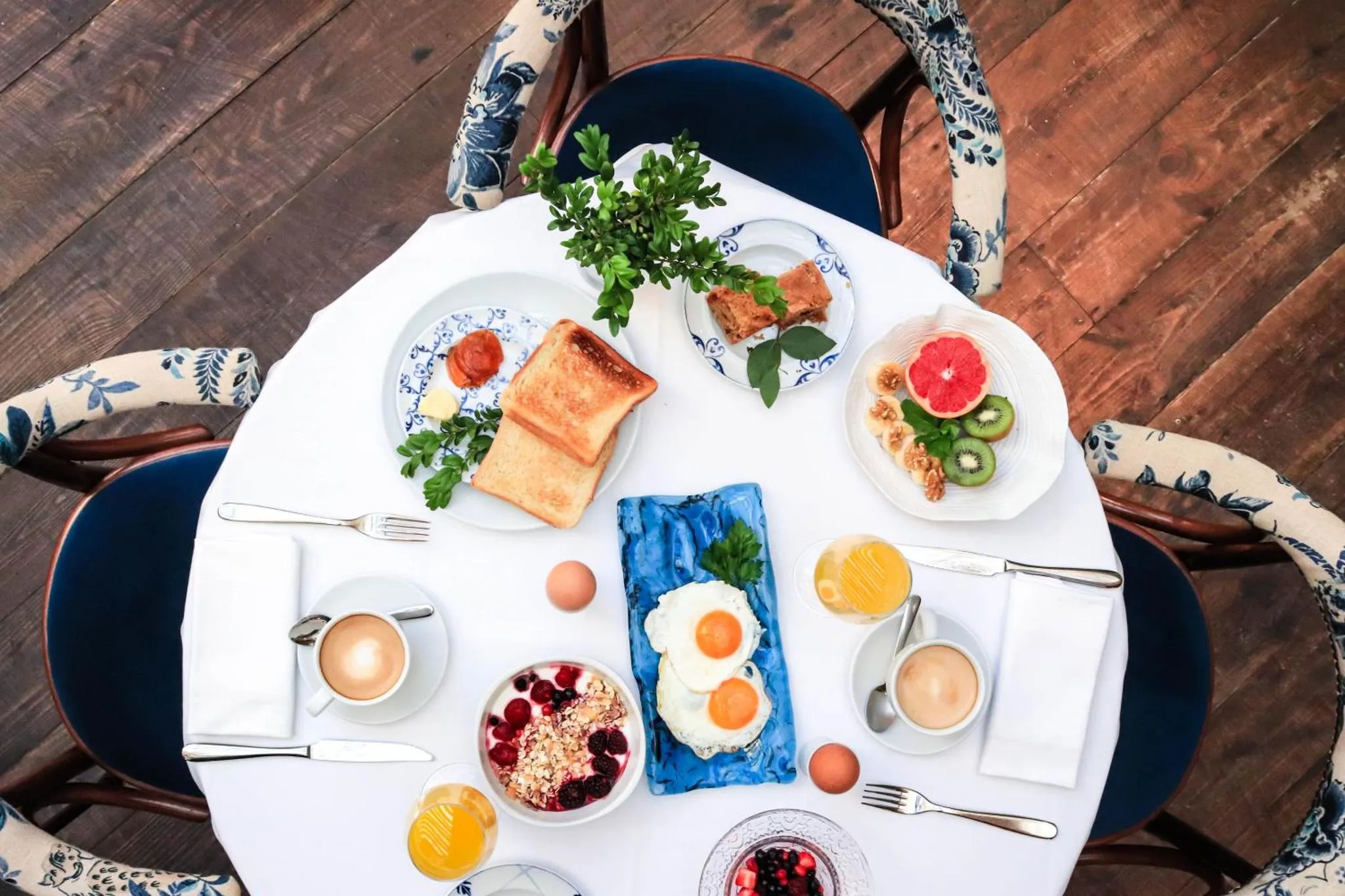 Une table ronde est dressée pour un repas avec des assiettes, des couverts et des boissons.