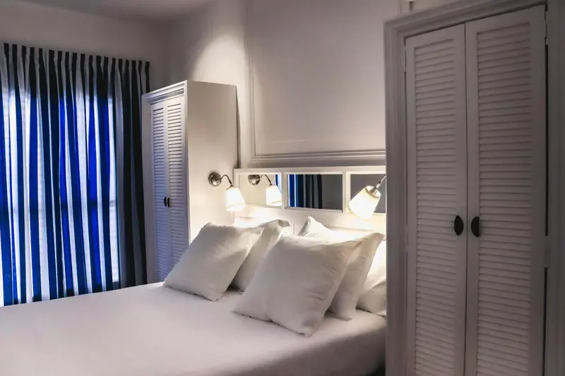 Une chambre lumineuse avec un lit recouvert d'oreillers blancs et un grand placard.