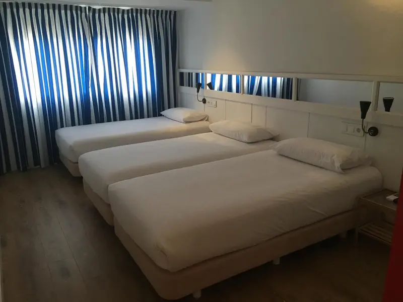 Chambre avec deux lits simples et rideaux bleus et blancs.