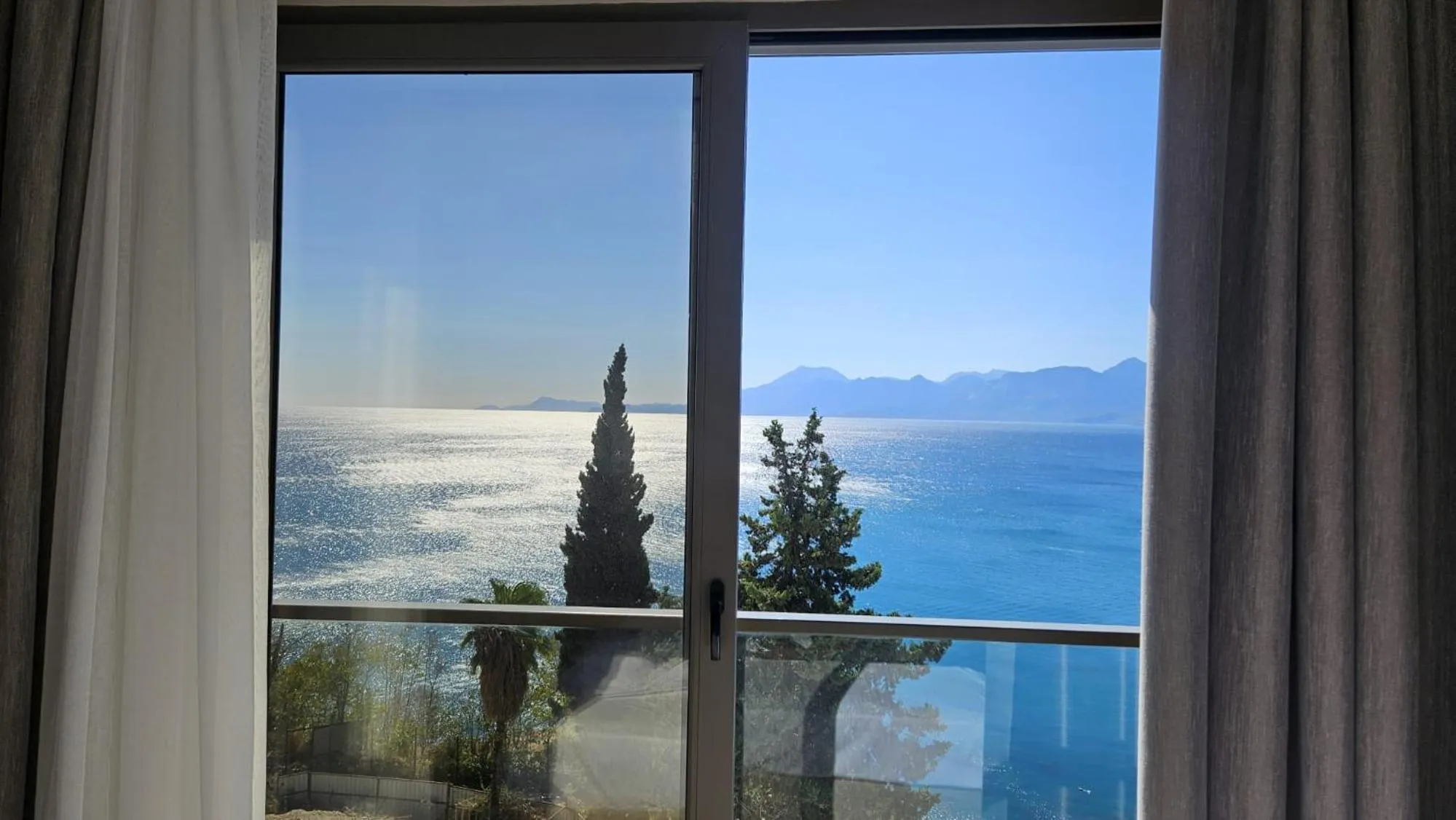 Vue sur la mer depuis une fenêtre avec rideaux.