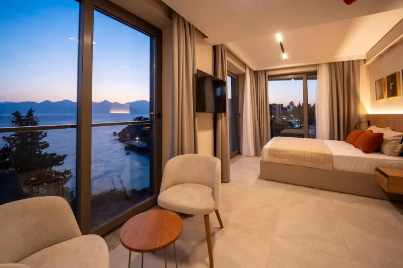 Chambre lumineuse avec coin salon et vue sur la mer au crépuscule.