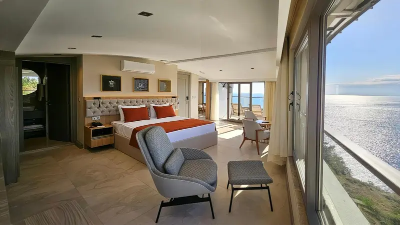 Chambre lumineuse avec un grand lit et un coin salon donnant sur la mer.