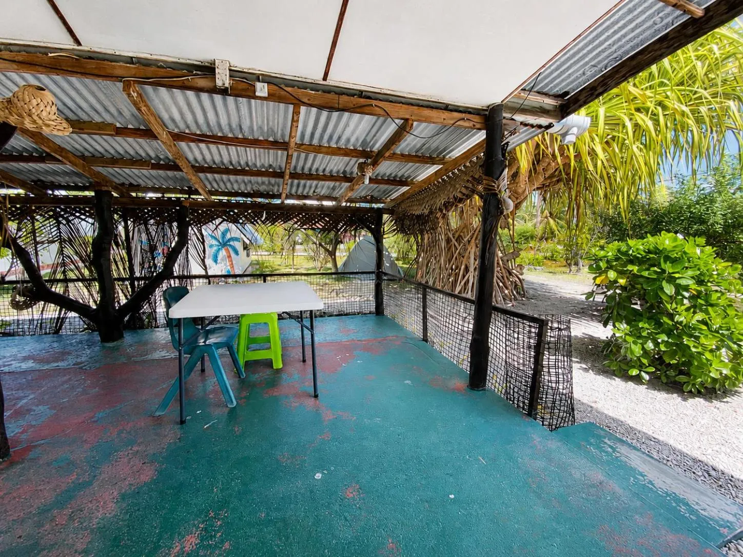 Une table et des chaises en plastique sont disposées sur une terrasse ombragée.