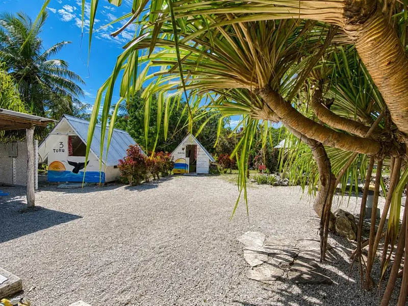 Des bungalows blancs aux toits inclinés se dressent sur un sol de gravier, ombragés par la végétation luxuriante.