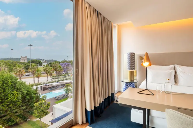 Chambre lumineuse avec vue sur un paysage verdoyant et une piscine.