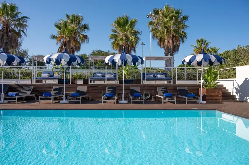 Terrasse avec transats et parasols au bord d'une piscine turquoise.