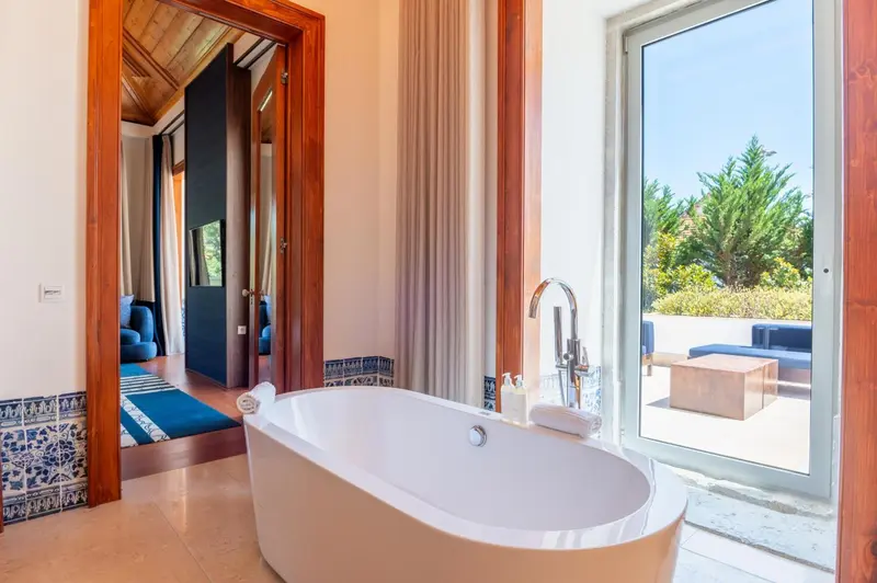 Une baignoire blanche se trouve dans une salle de bain lumineuse avec une vue sur une terrasse.