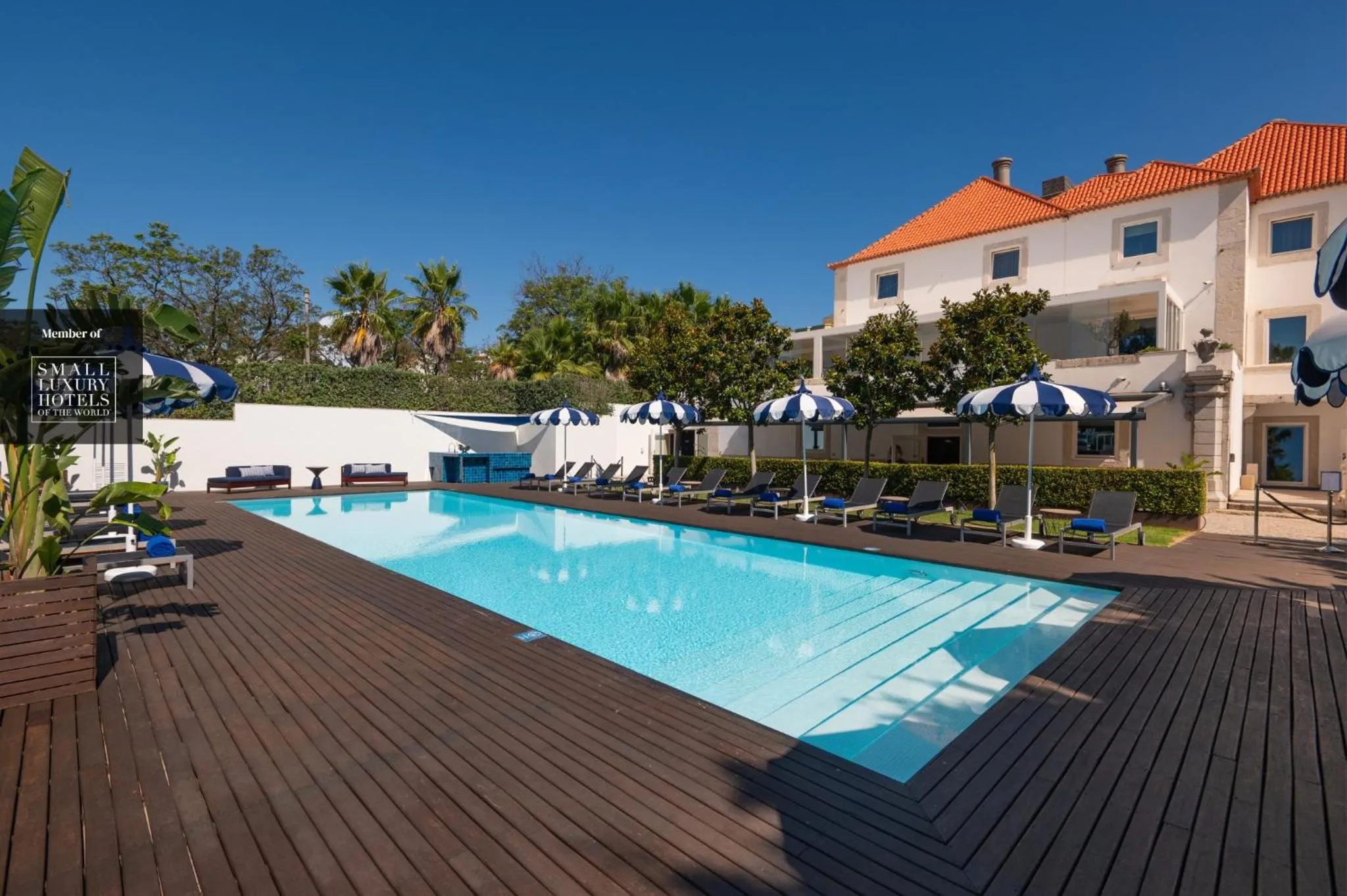 Une piscine rectangulaire bordée d'une terrasse en bois, avec des transats et des parasols.